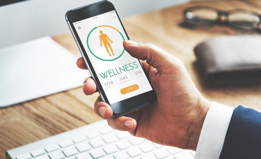 a man’s hand holding a smartphone with an open health diet app and a keyboard in the background