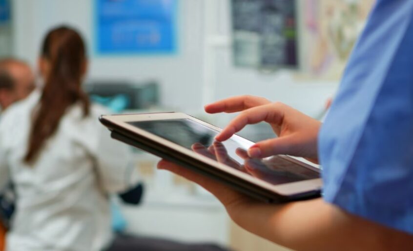 hands of a nurse using a tablet with medical staff in the background