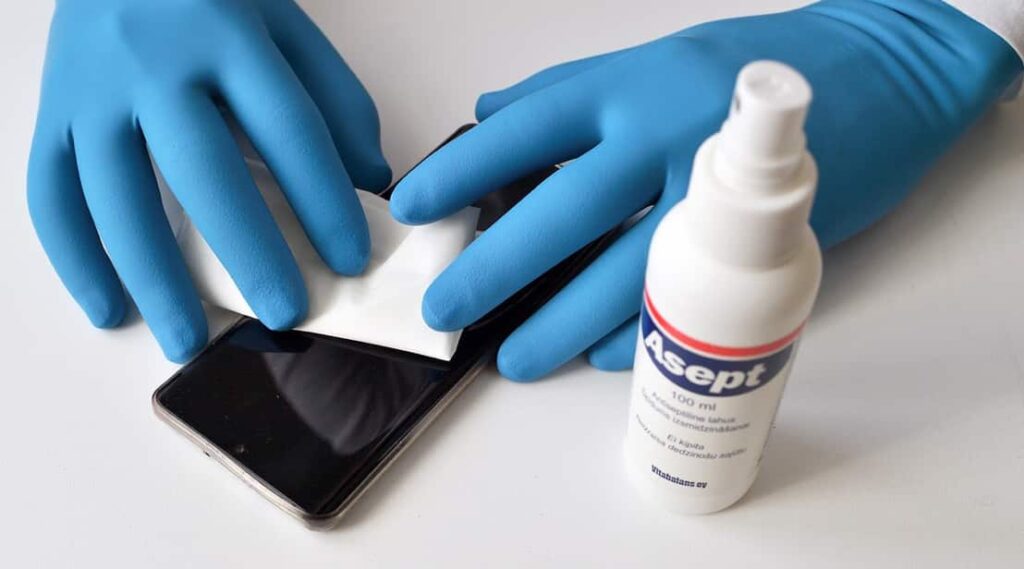 Hands with blue gloves sanitizing a smartphone