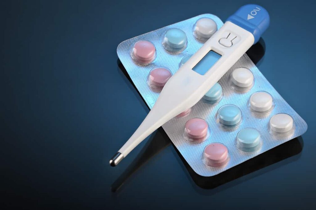 Digital thermometer and pills on blue background