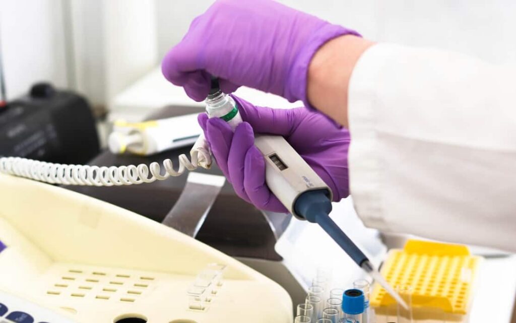 Gloved hand operating a pipette in a lab