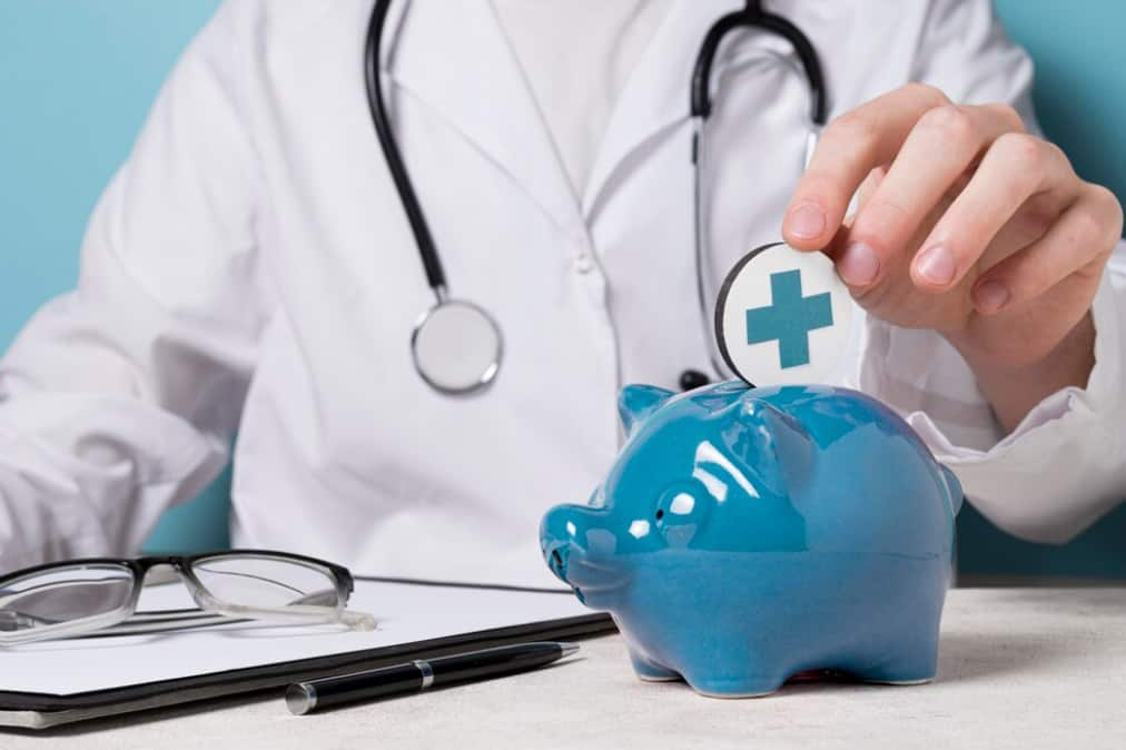 a doctor in medical white suit putting a coin  with croos into blue piggy bank