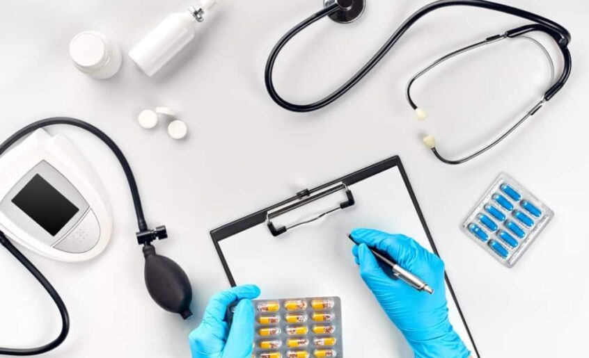 doctor's gloved hands holding a pen over a clipboard, with medical equipment around