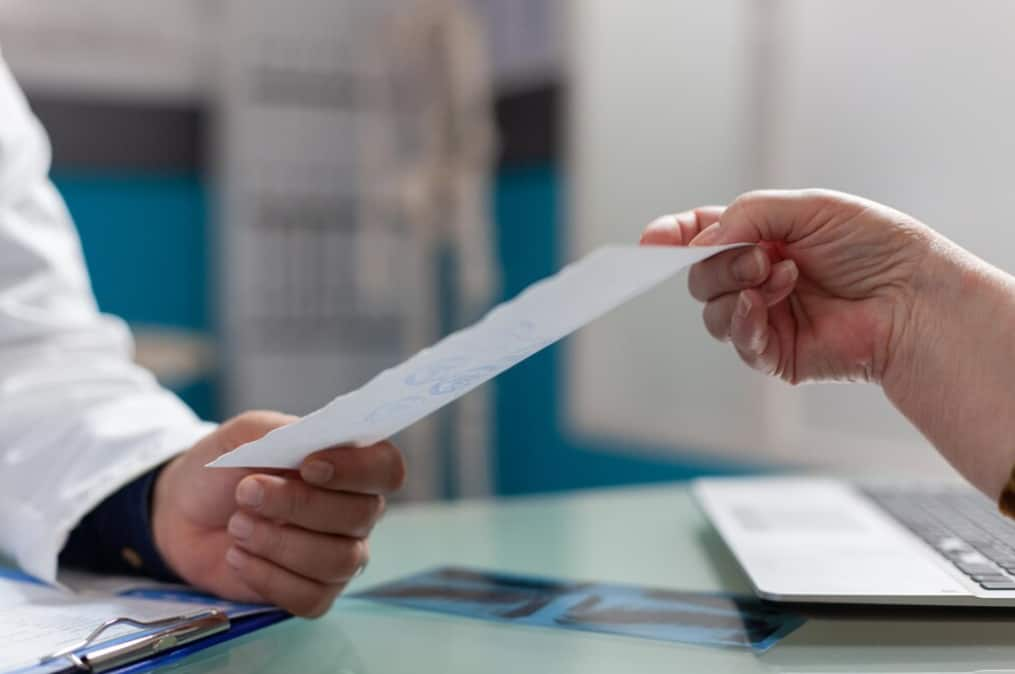 A doctor's hand giving a paper to a patient in a clinical setting