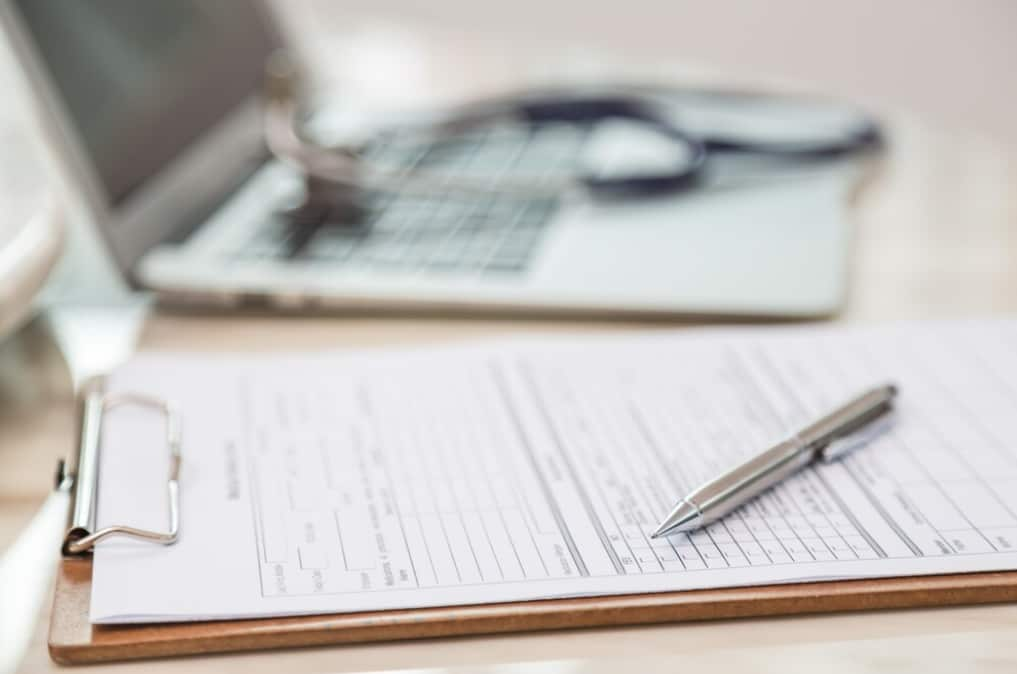 A blurred background focusing on a medical form beside a laptop and stethoscope