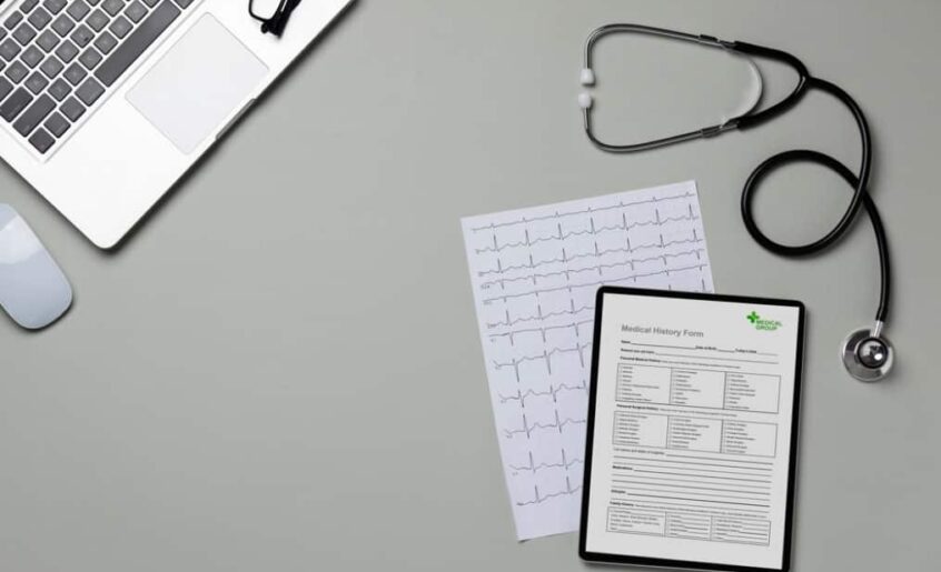 A laptop, stethoscope, EKG printout, and medical form on a des